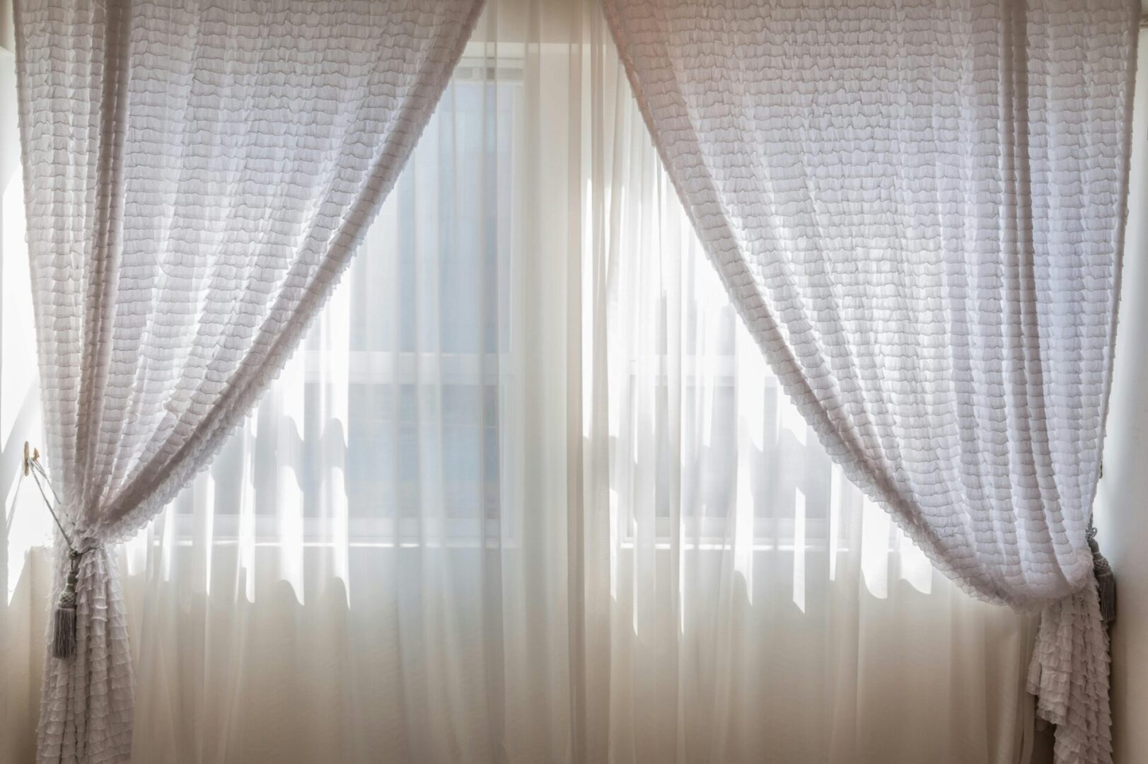 A window with white curtains and blinds in the room.